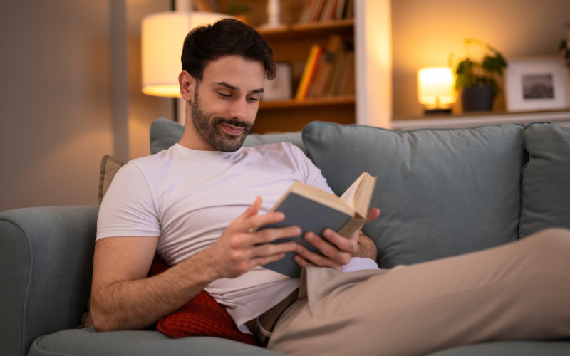 ​Estudiante de Contaduría Pública virtual relajado leyendo en el sofá de su casa​