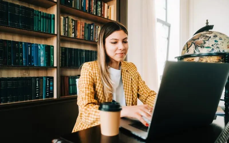 Profesional estudia marketing en línea desde su espacio de trabajo con un computador portátil y apuntes.