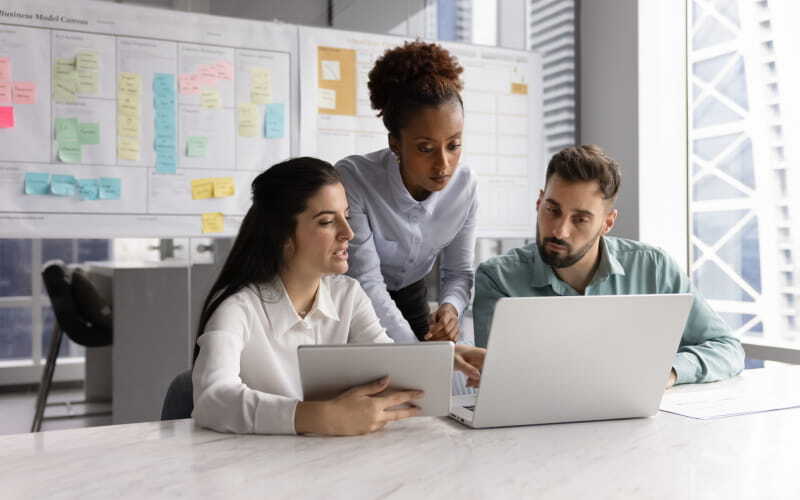 ​Tres profesionales en Marketing en su oficina validan data en laptop para presentar informes del rendimiento de la compañía​