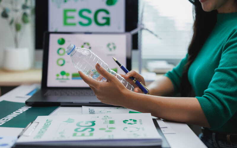 Profesional de la Maestría en Desarrollo Sostenible realiza una estrategia ESG en su oficina mientras revisa una botella de plástico