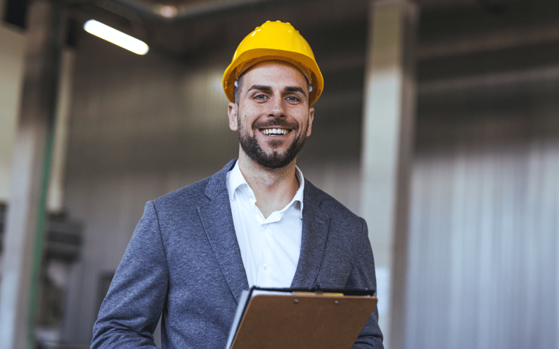 ​Profesional sonriente con casco se encuentra en campo en proceso de verificación de las medidas de seguridad y salud laboral​.